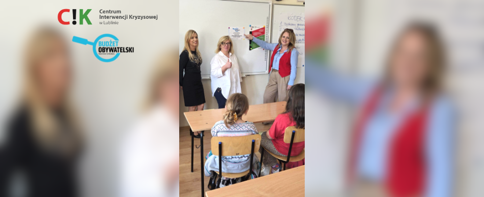 3 kobiety stoją przy tablicy w sali szkolnej i prowadzą zajęcia dla dzieci. widoczne od tyłu 2 postacie dzieci siedzące w ławce szkolnej