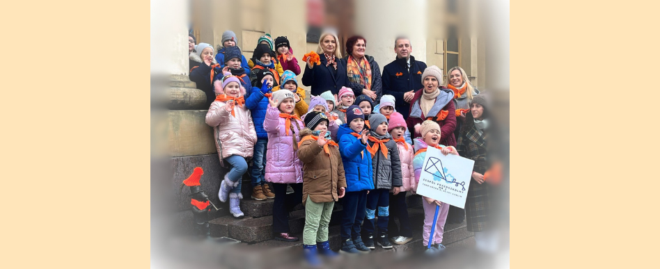 grupa dzieci i dorosłych ubranych w pomarańczowe szaliki stoją na schodach budynku