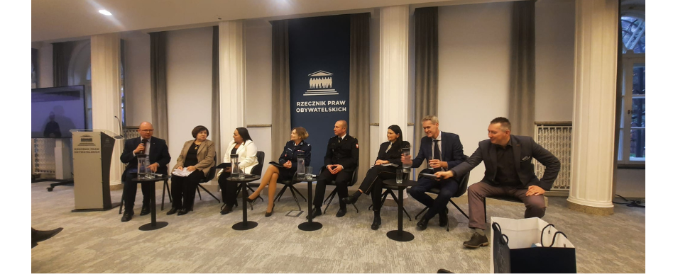 wnętrze sali konferencyjnej, uczestnicy siedzący obok siebie, w tle napis biuro rzecznika praw obywatelskich